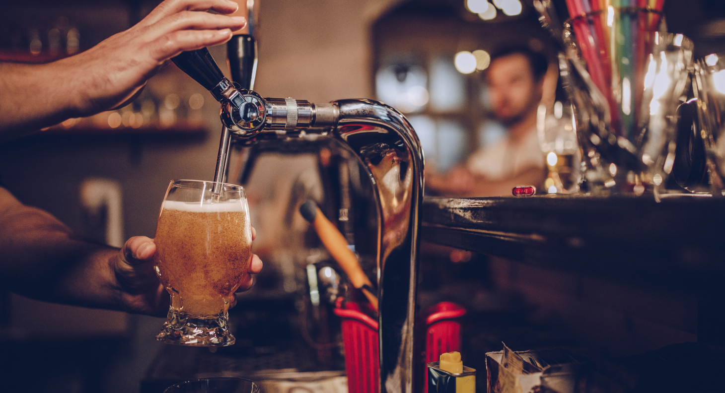 Man in pub pouring beer into glass from tap