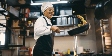 Happy chef wearing hat and apron tossing stir fry in pan