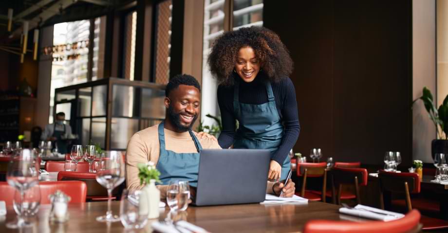 Restaurant managers smiling, working with laptop inside of restaurant before it opens